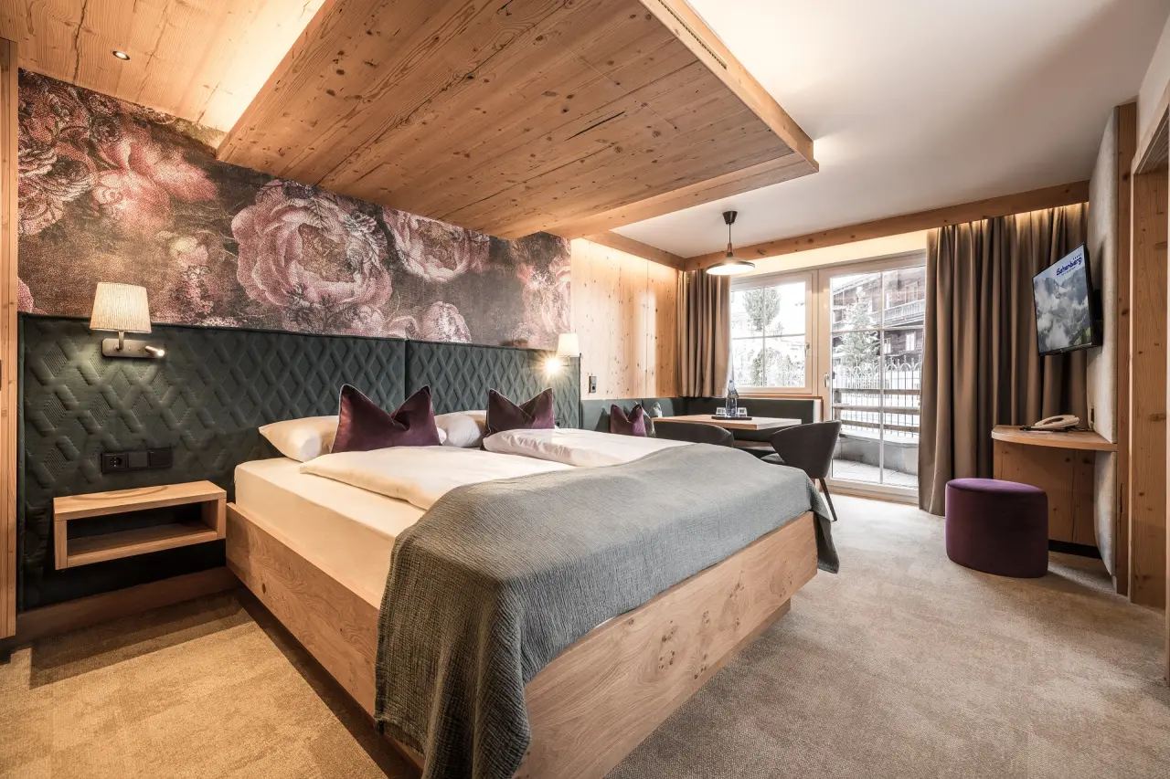 Gemütliches Doppelzimmer mit Holzelementen, floraler Wandgestaltung und Sitzbereich im Galtenberg Resort 4*S.