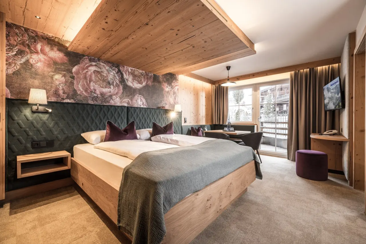 Modernes Doppelzimmer mit Holzelementen, floraler Wand und Sitzbereich im Galtenberg Resort 4*S.