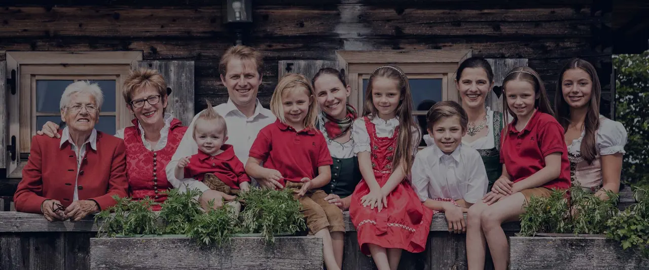 Die Gastgeberfamilie des Gipfelhaus Magdalensberg in traditioneller Tracht vor dem rustikalen Holzgebäude, symbolisiert herzliche Gastfreundschaft.