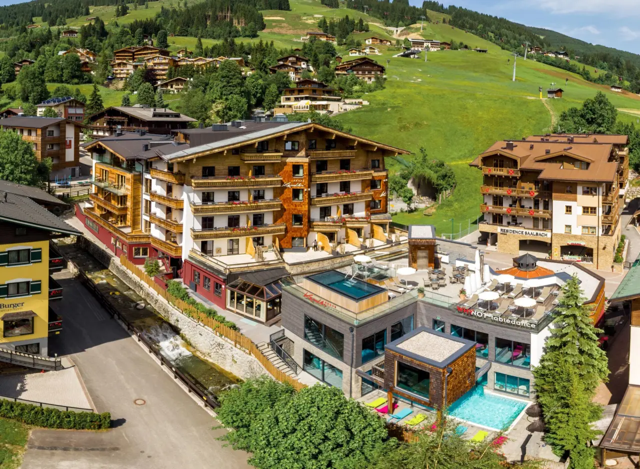 Luftaufnahme des Hotel Kendler in Saalbach mit Aussenpools und Bergblick. Modernes Wellnesshotel in alpiner Landschaft.