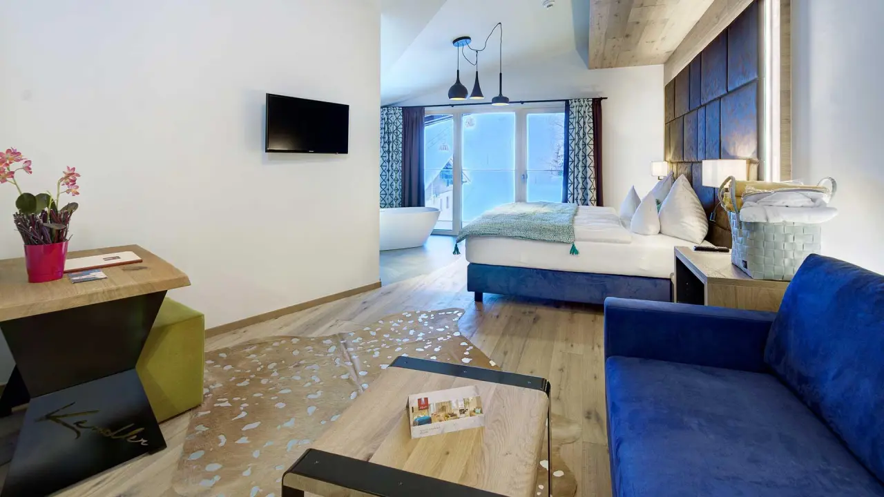 Modernes Hotelzimmer im Hotel Kendler mit freistehender Badewanne am Fenster, Doppelbett und gemütlicher Sitzecke.