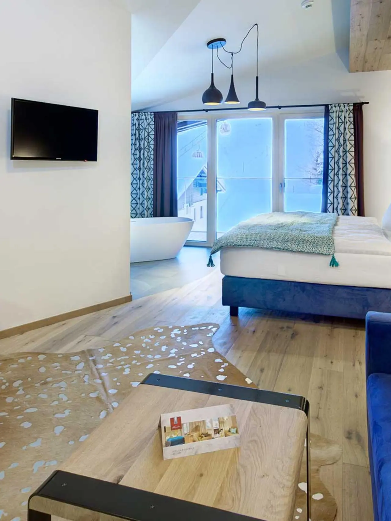 Modernes Hotelzimmer im Hotel Kendler mit Doppelbett, freistehender Badewanne, Holzboden und TV.