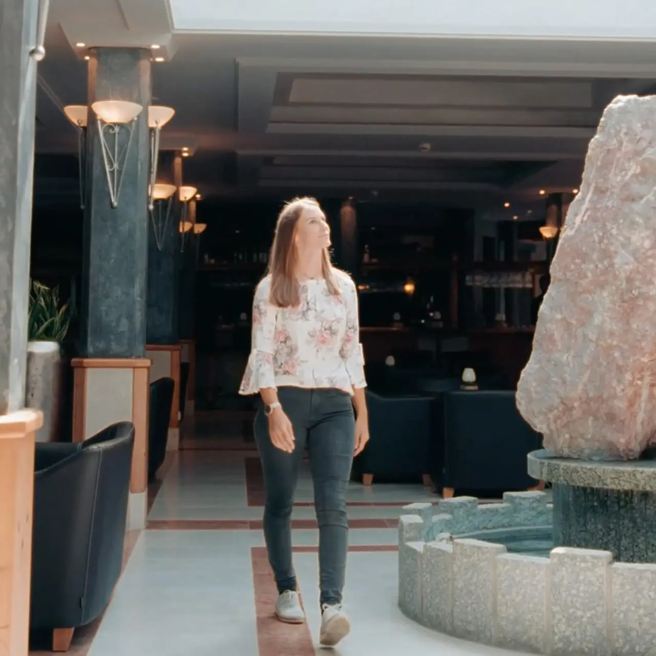 Frau geht durch die helle Lobby mit Steinbrunnen im Dolomiten Residenz Sporthotel Sillian.