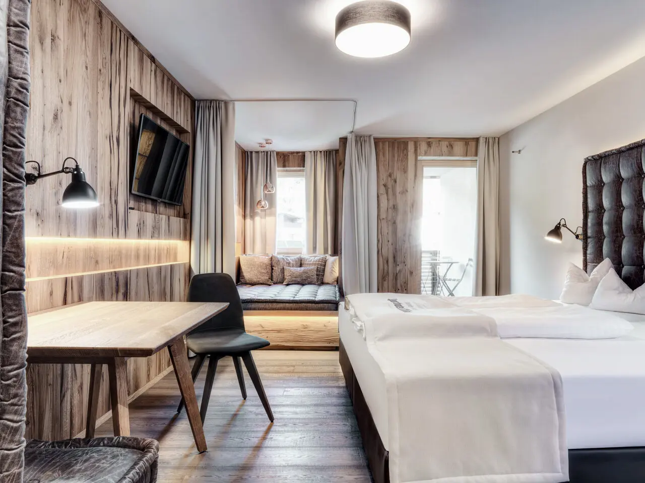 Modernes Doppelzimmer mit Holzelementen, Balkon und gemütlicher Sitzecke im Dolomiten Residenz Sporthotel Sillian.