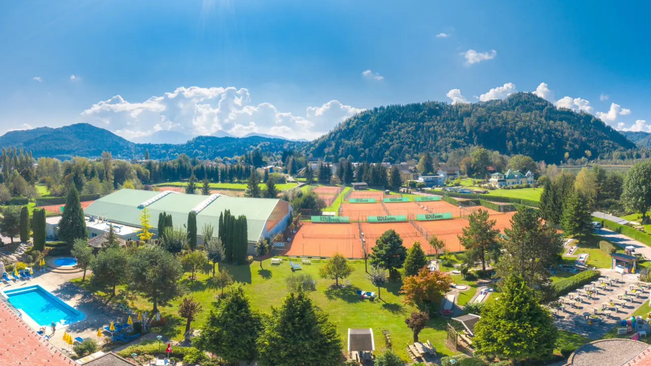 Weitläufige Anlage des Golf-Tennis-Wellnesshotel Mori mit Tennisplätzen, Pool und grüner Landschaft unter blauem Himmel.