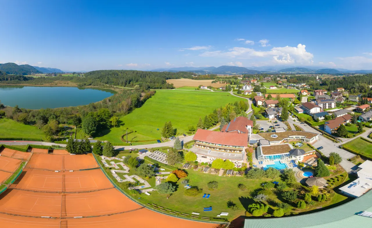 Luftbild des Golf-Tennis-Wellnesshotel Mori mit Außenpool, Tennisplätzen, See und Alpenpanorama.