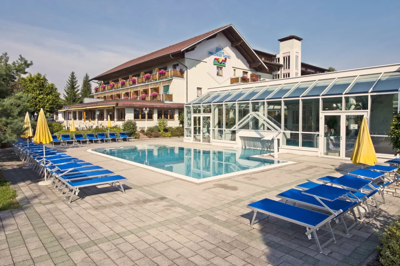 Aussenpool mit blauen Liegestühlen und angrenzendem Glasbau des Innenpools im Golf-Tennis-Wellnesshotel Mori.