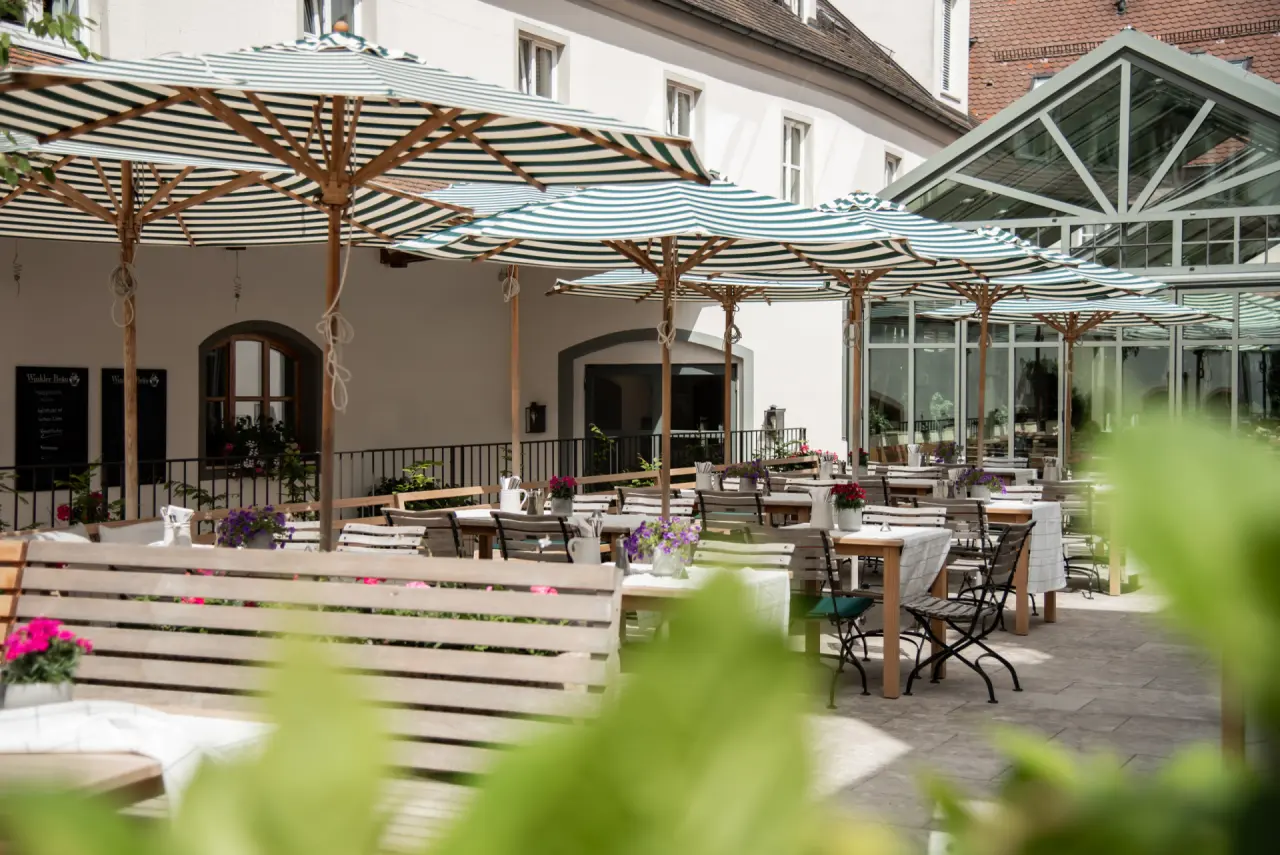 Sonniger Restaurant-Garten mit gestreiften Sonnenschirmen und Holztischen im Winkler Bräu Gutshofhotel.