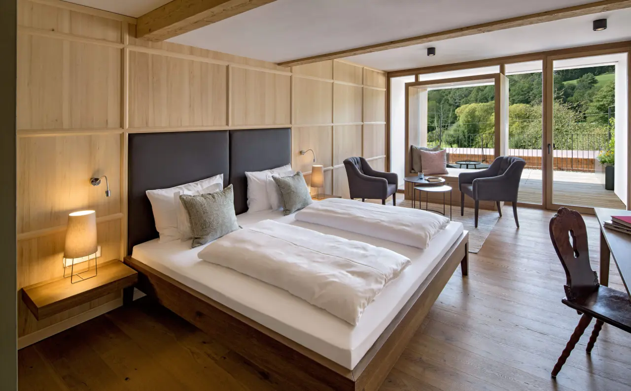 Geräumiges Doppelzimmer mit Holzelementen, gemütlicher Sitzecke und Balkon mit Waldblick im Winkler Bräu Gutshofhotel.
