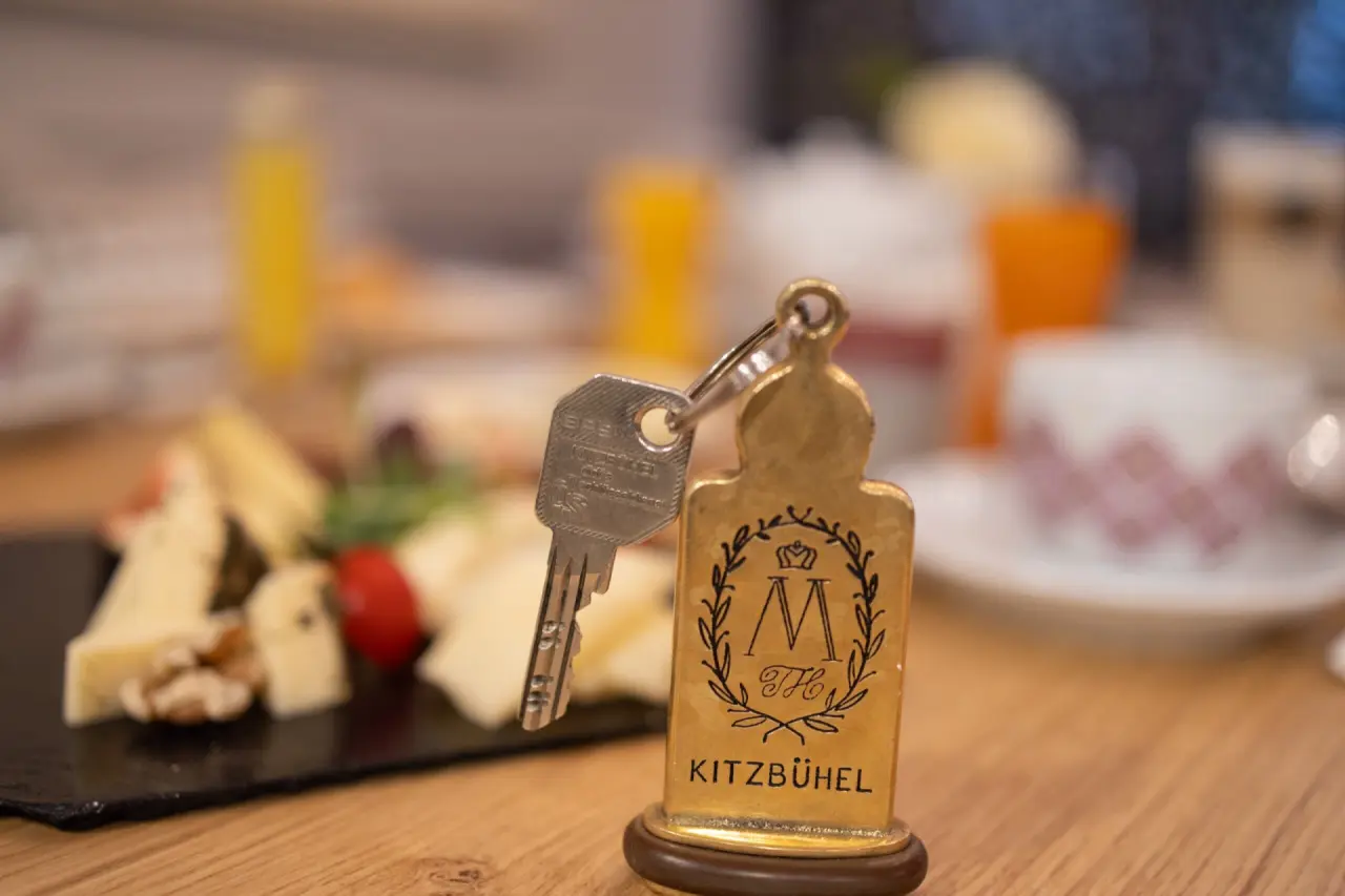 Q! Hotel Maria Theresia Kitzbühel in Kitzbühel – Hotelschlüssel mit Logo und Frühstück im Hintergrund | Wellnesshotel Tirol