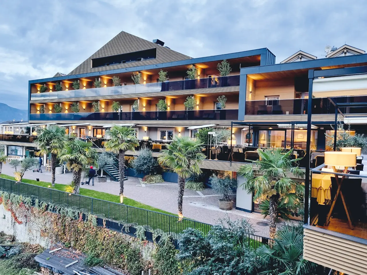 Weinegg Wellviva Resort in Girlan – Moderne Außenansicht mit beleuchteten Balkonen und Palmen | Wellnesshotel Südtirol