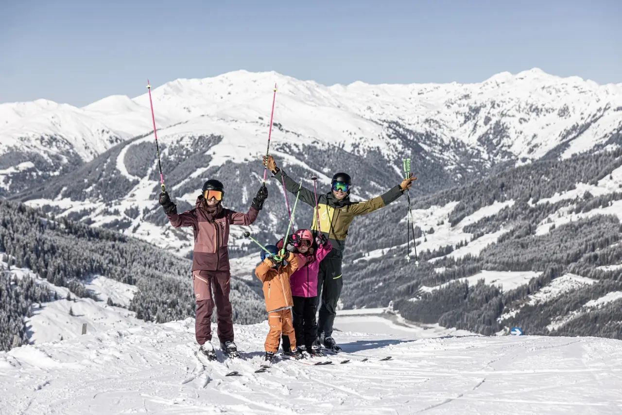 Glückliche Familie beim Skifahren mit verschneitem Bergpanorama im Zillertal. Winterurlaub im Mari Pop Hotel Zillertal.