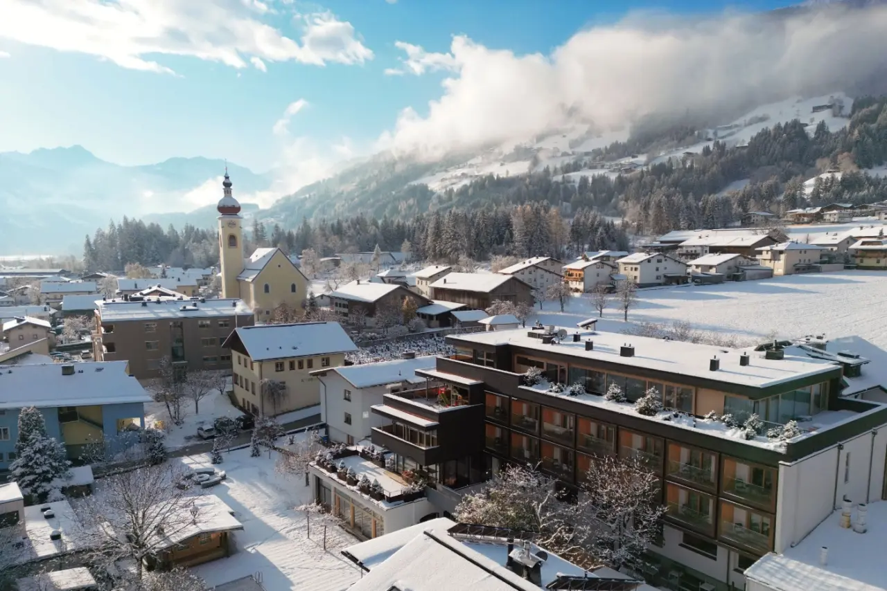 Winterliche Luftaufnahme des Mari Pop Hotel Zillertal im verschneiten Dorf mit Kirche und Alpenpanorama.