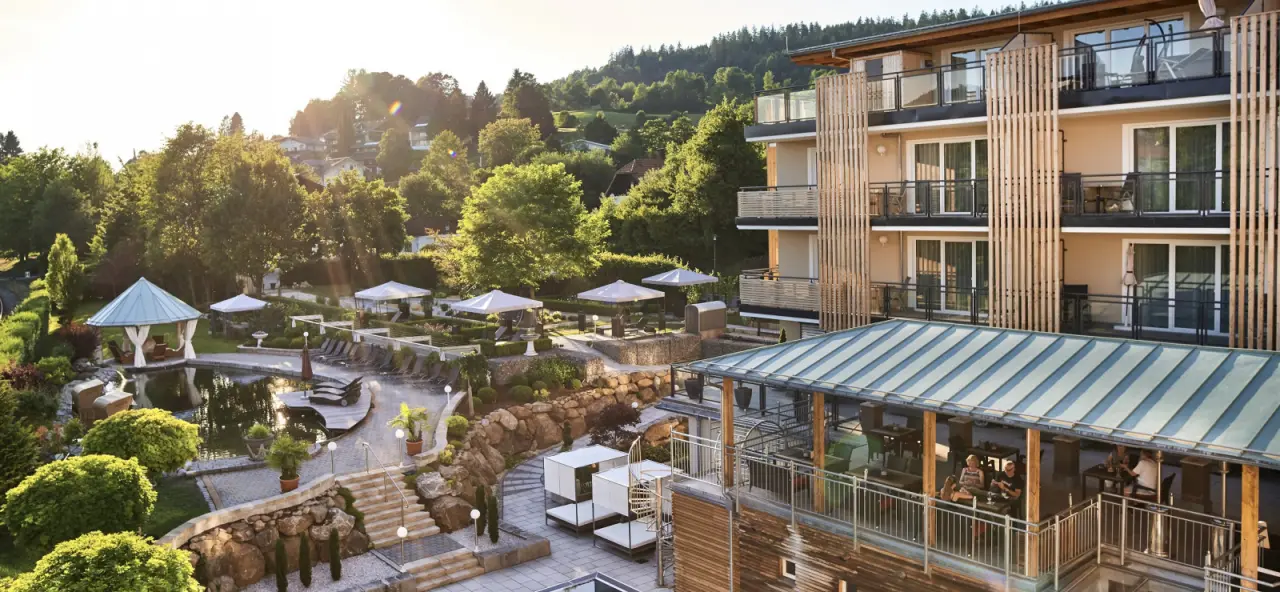 Panoramablick auf den Bodenmaiser Hof mit Hotelgebäude, weitläufiger Gartenanlage und Naturbadeteich im Abendlicht.