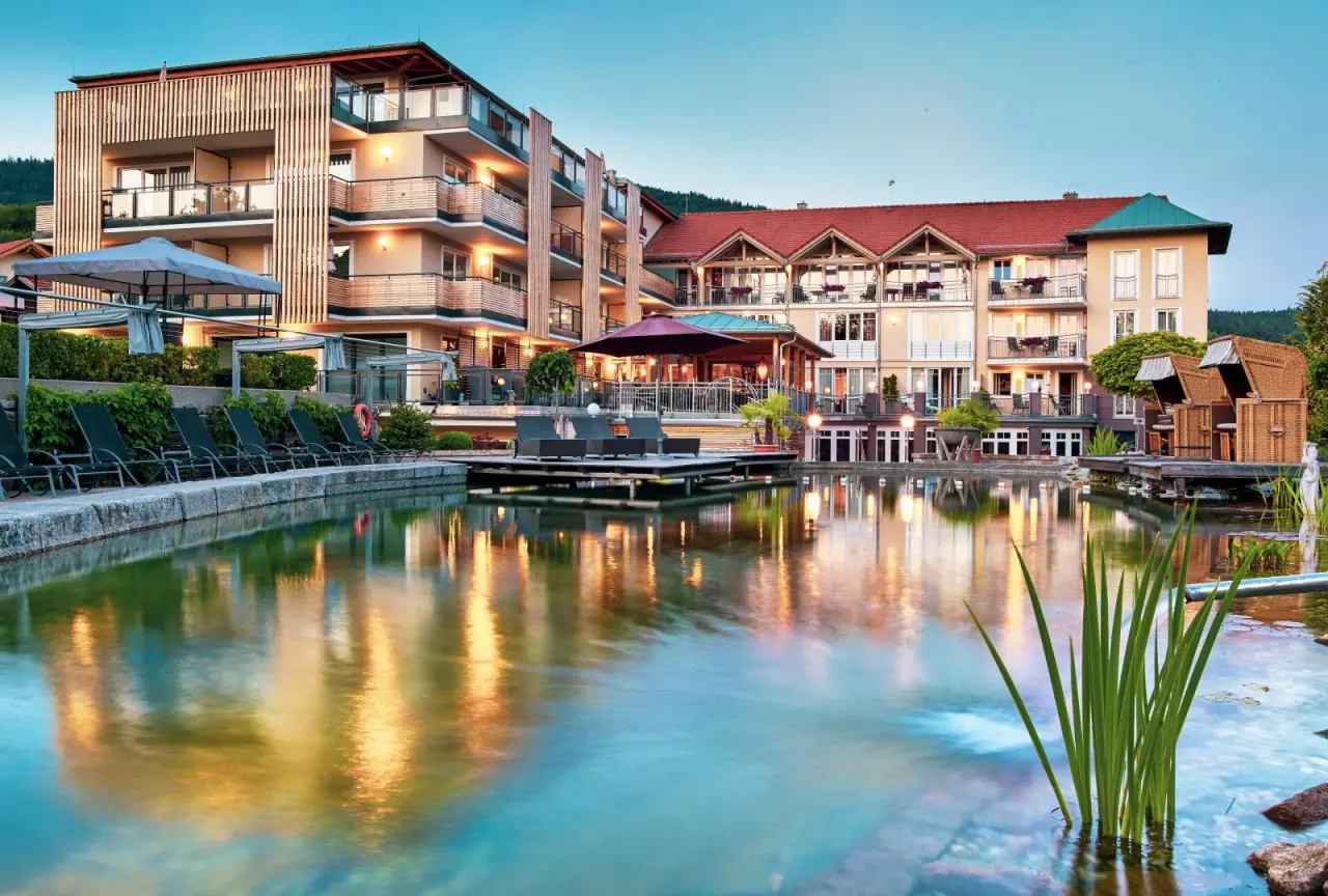Abendstimmung am Naturbadeteich des Bodenmaiser Hofs mit beleuchteter Hotelanlage und Liegebereich.