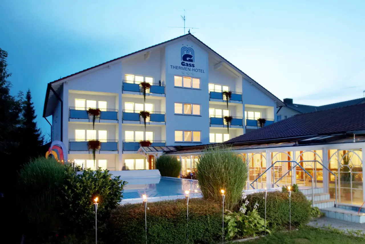 Aussenansicht des Thermenhotel Gass in Bad Füssing bei Abenddämmerung mit beleuchteten Fenstern und Poolbereich.