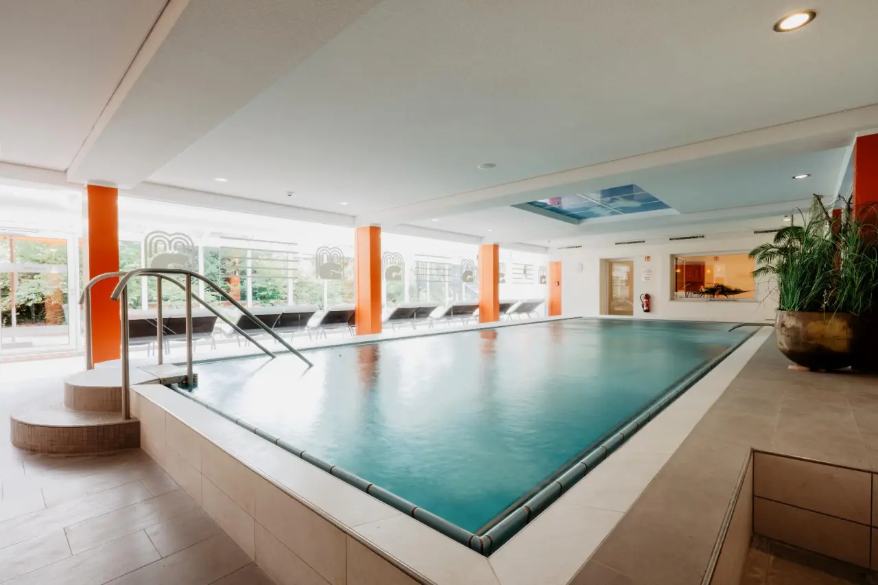 Helles Innenbecken im Thermenhotel Gass, Bad Füssing mit Liegen und Blick ins Grüne für entspannte Stunden.