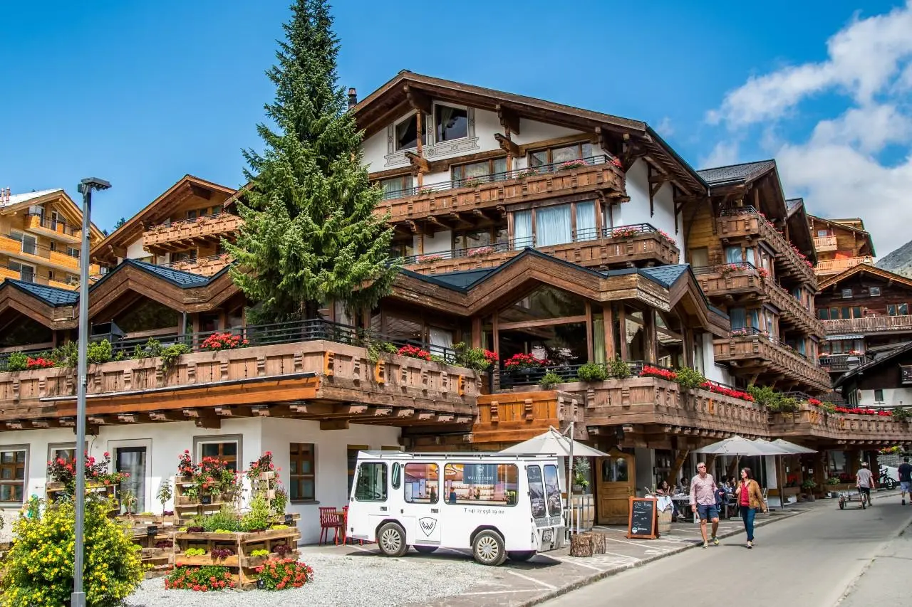 Aussenansicht des Walliserhof Grand-Hotel & Spa mit traditioneller Holzarchitektur, Balkonen und Blumen in den Schweizer Alpen.