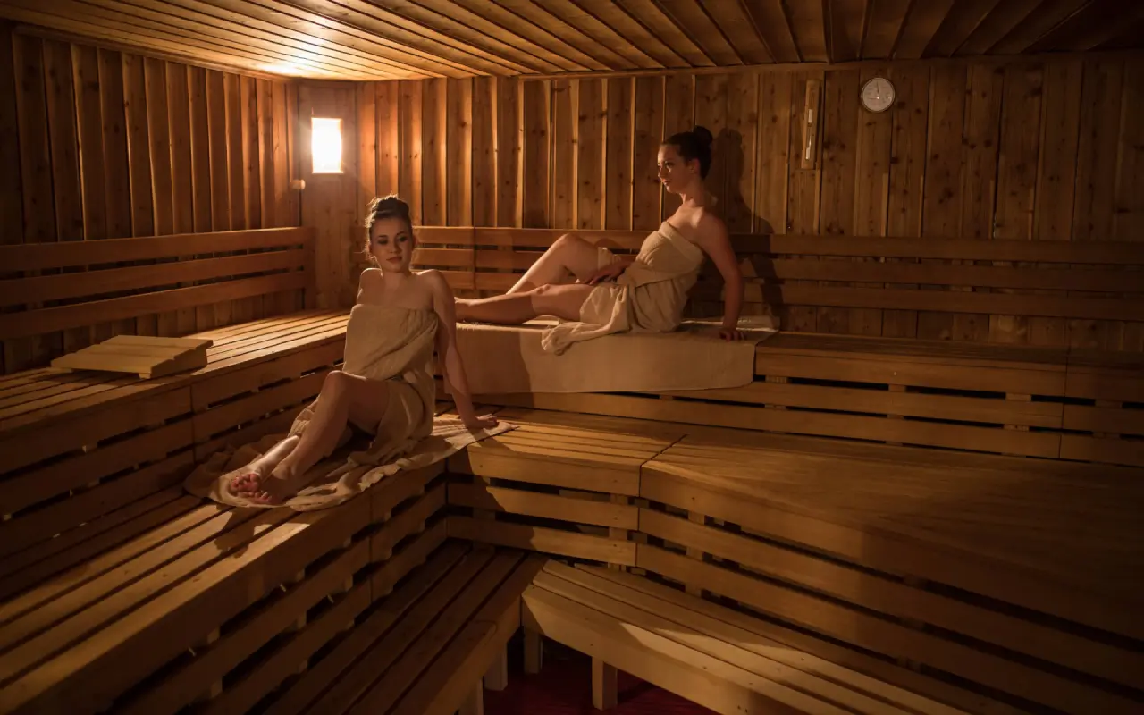 Zwei Frauen entspannen in der finnischen Sauna des Walliserhof Grand-Hotel & Spa, umgeben von warmem Holz und sanftem Licht.