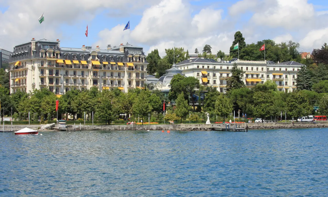 Grandhotel Beau Rivage Palace am Genfersee mit prächtiger Fassade, gelben Markisen und üppigem Grün am Ufer.