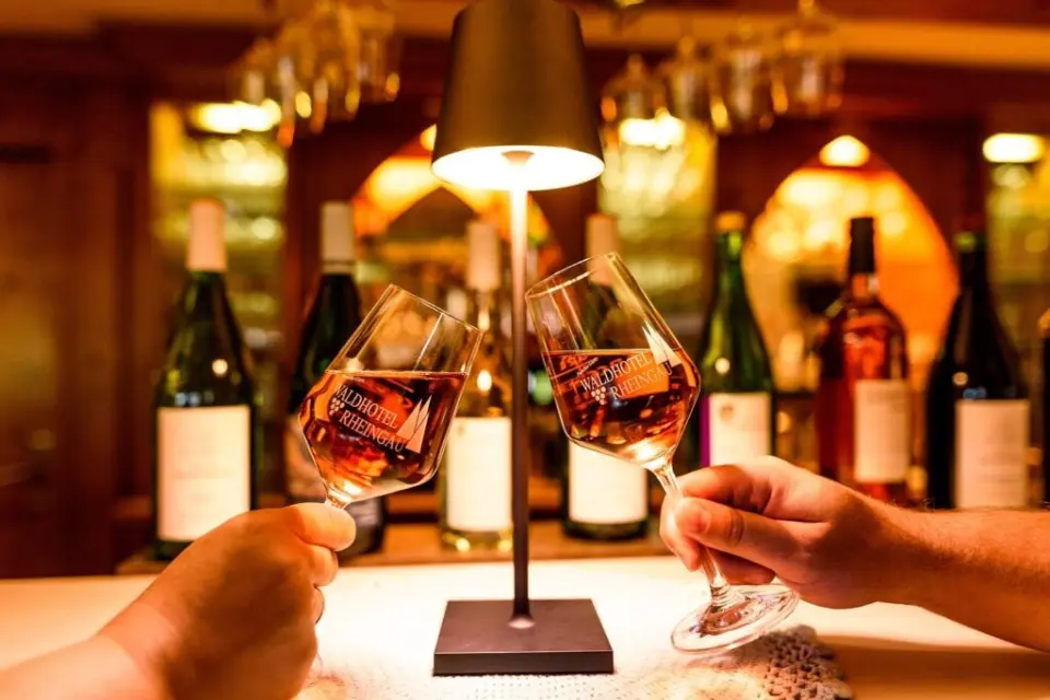 Zwei Weingläser mit Hotel-Logo stoßen an der gemütlichen Bar des AKZENT Waldhotel Rheingau an.