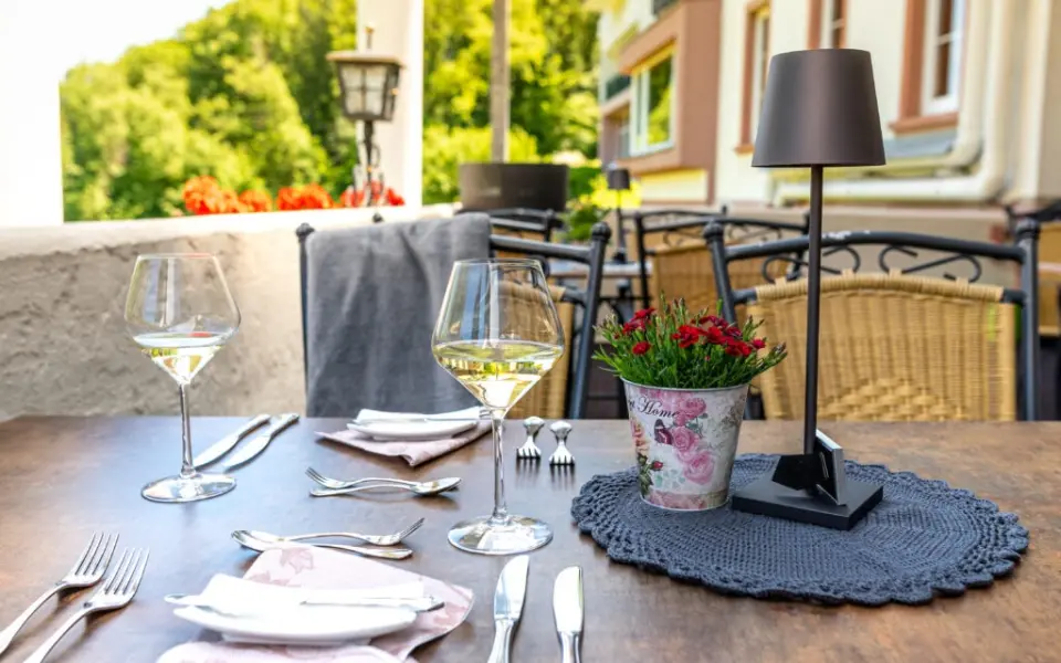 Gedeckter Tisch mit Weingläsern und Blumen auf der Terrasse des AKZENT Waldhotel Rheingau, umgeben von grüner Natur.