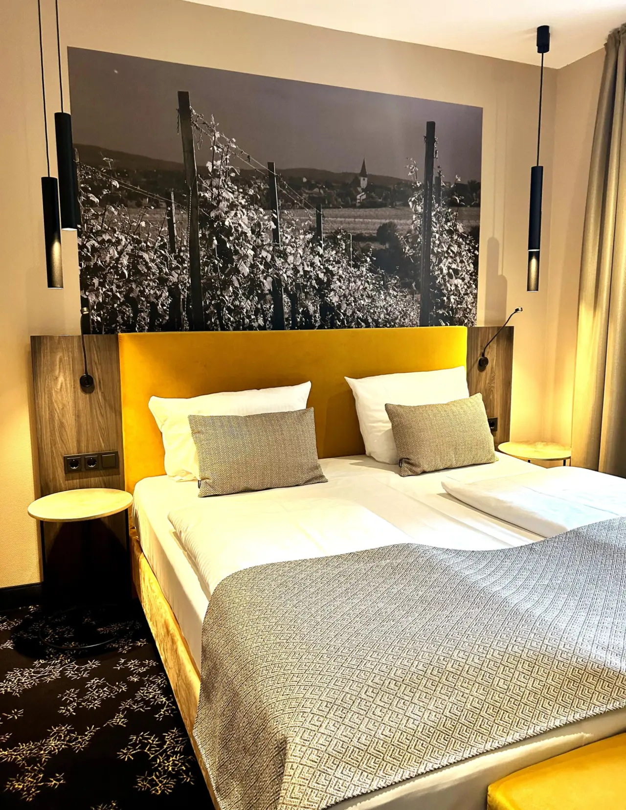 Modernes Doppelzimmer mit gelbem Kopfteil und Weinbergs-Wandbild im AKZENT Waldhotel Rheingau.