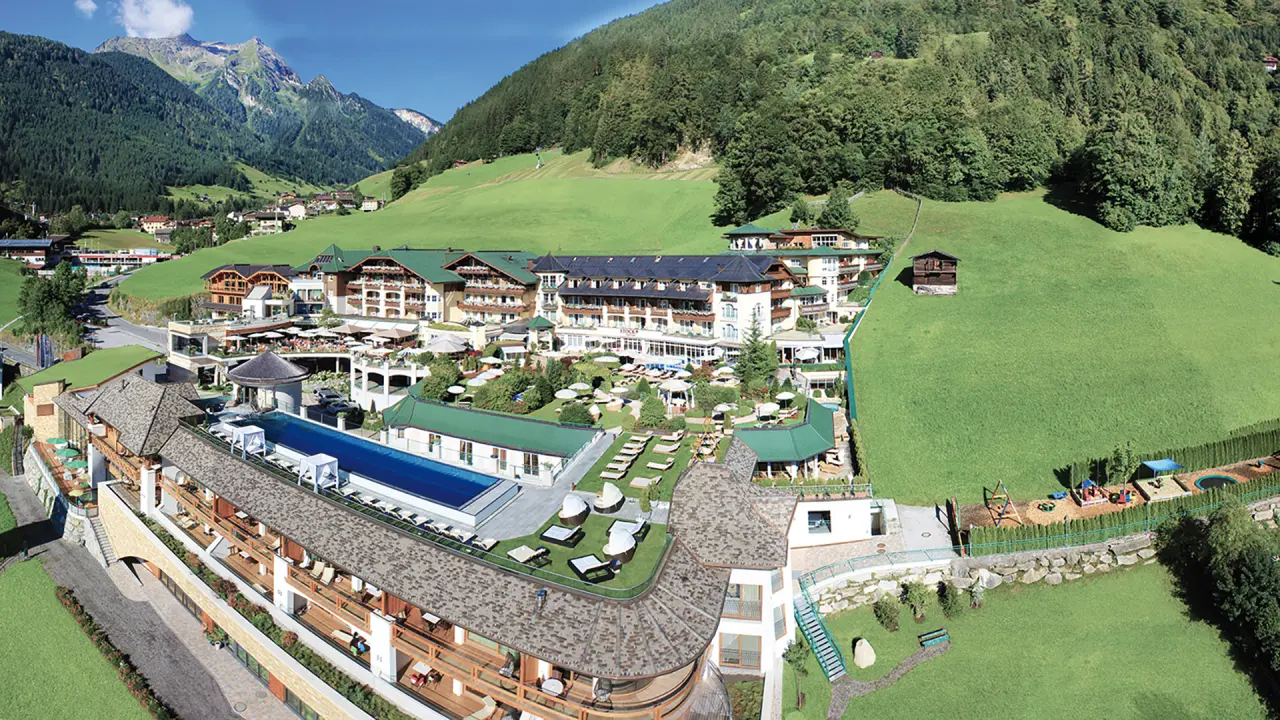 Luftaufnahme des STOCK resort *****s in den Zillertaler Alpen mit Hotelanlage, Infinity Pool und grünen Bergwiesen.