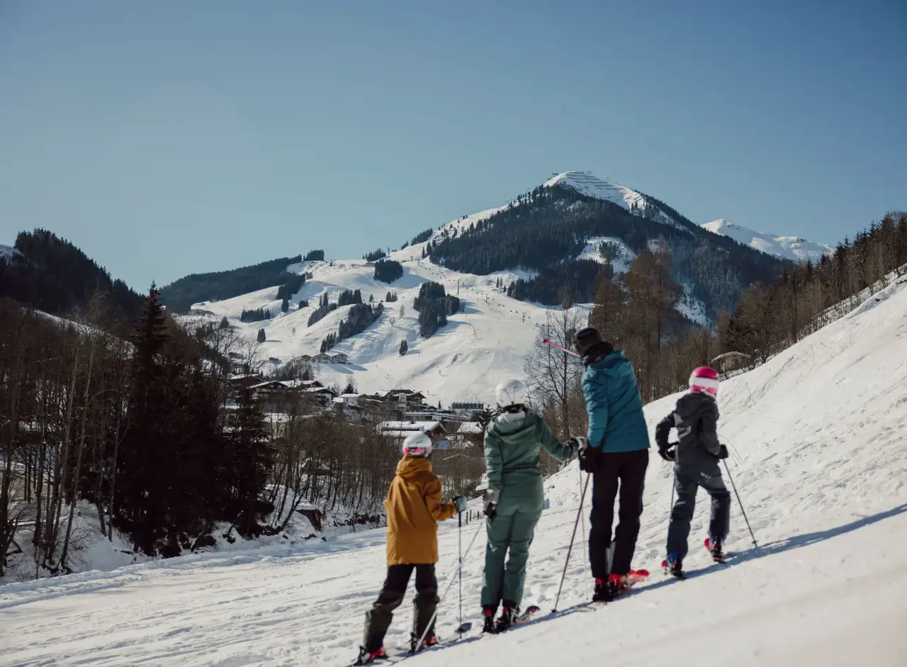 Familie beim Skifahren mit Blick auf die verschneite Berglandschaft und Skipisten beim Familien- & Gartenhotel Theresia.