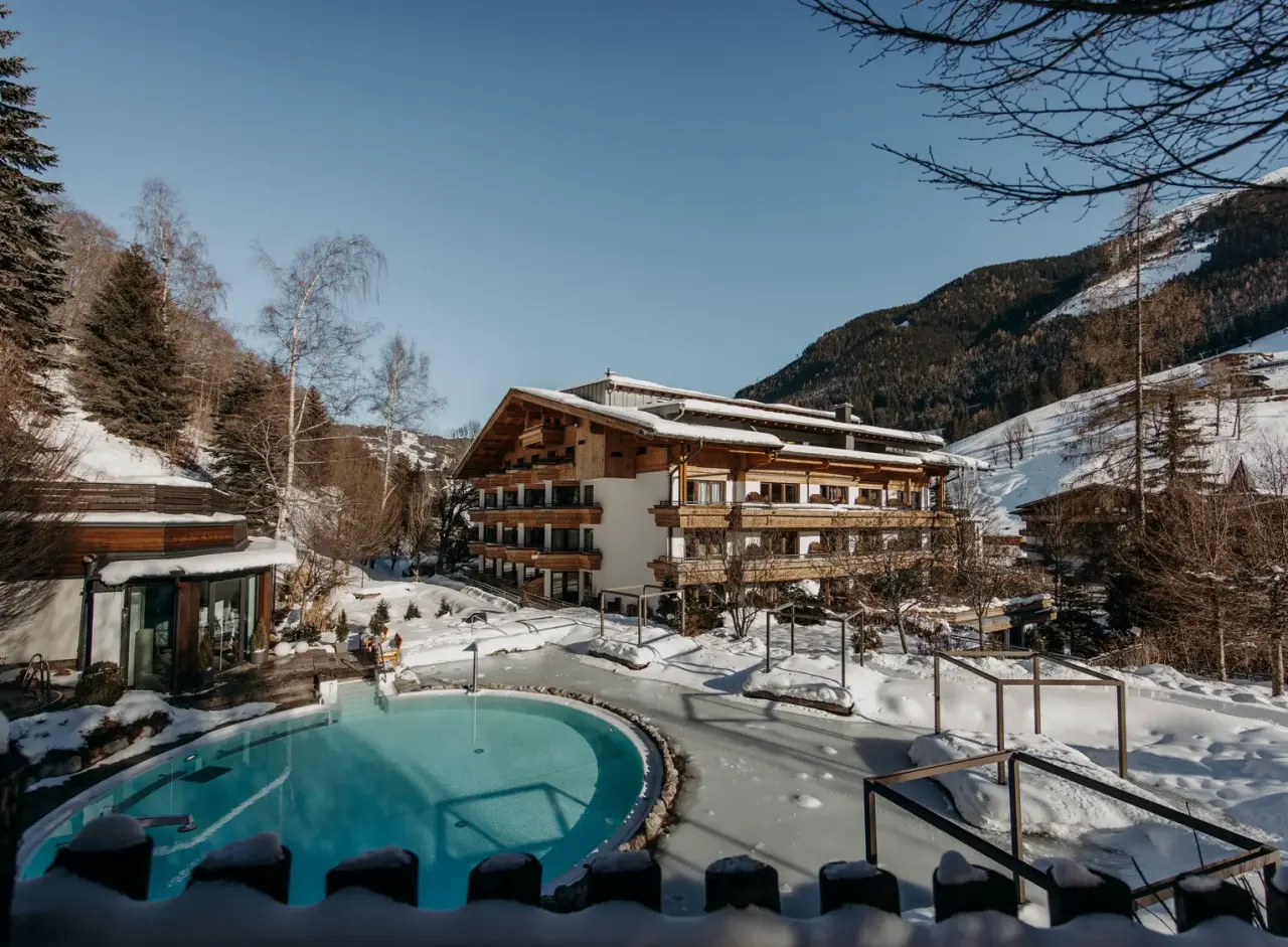 Familien- & Gartenhotel Theresia****S: Beheizter Aussenpool im Schnee mit Alpenpanorama und traditioneller Holzarchitektur.