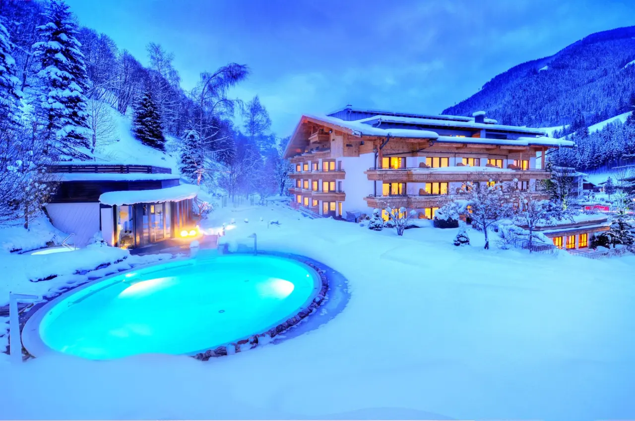 Beleuchteter Aussenpool und verschneites Familien- & Gartenhotel Theresia****S bei Dämmerung in den Alpen.