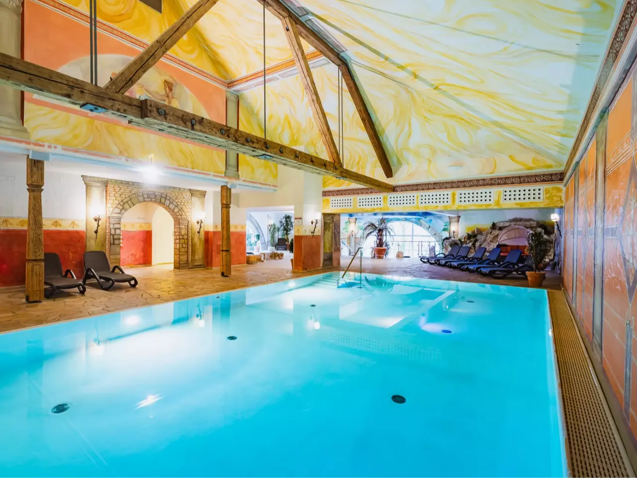 Grosszügiger Innenpool mit kunstvoll bemalter Decke und Liegebereich im Reiterhof Bellevue Spa Resort Wirsberg.