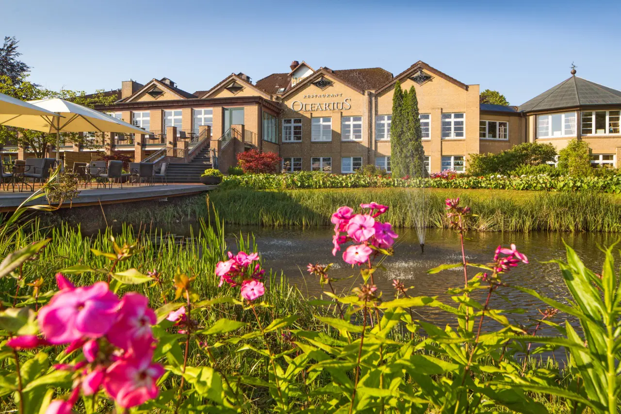 Idyllisches Hotel Waldschlösschen mit Restaurant Olearius, umgeben von einem blühenden Garten mit Teich und Sonnenterrasse.