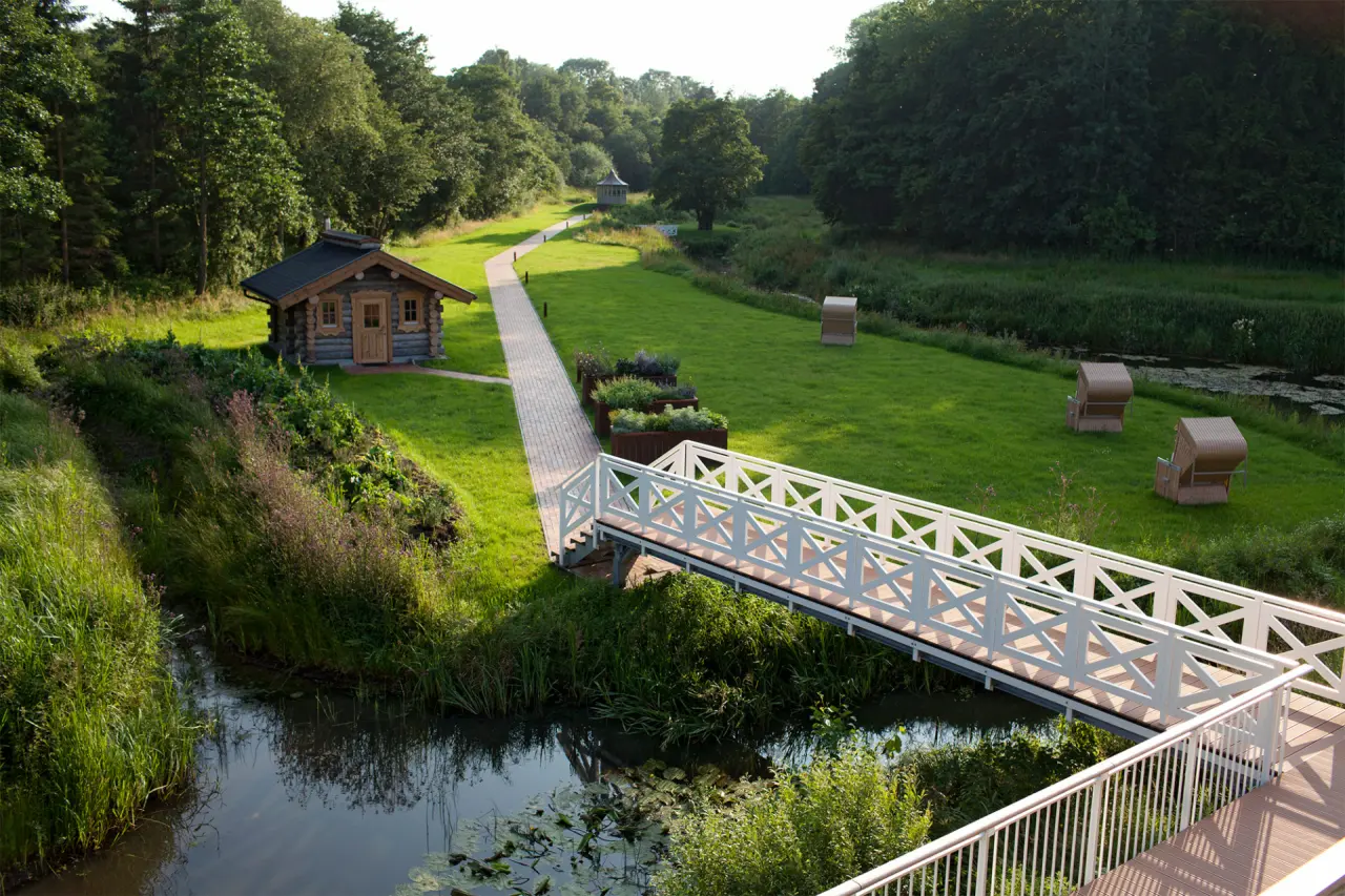 Idyllischer Wellness-Garten im Hotel Waldschlösschen mit Saunahütte, Holzbrücke, Bach und Strandkörben zur Entspannung.