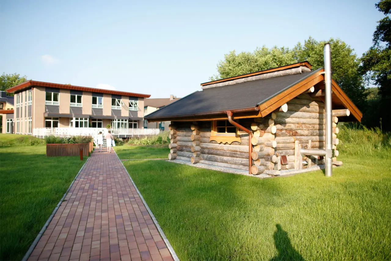 Traditionelle Blockhaus-Sauna im grünen Garten des Hotel Waldschlösschen mit Hauptgebäude im Hintergrund.