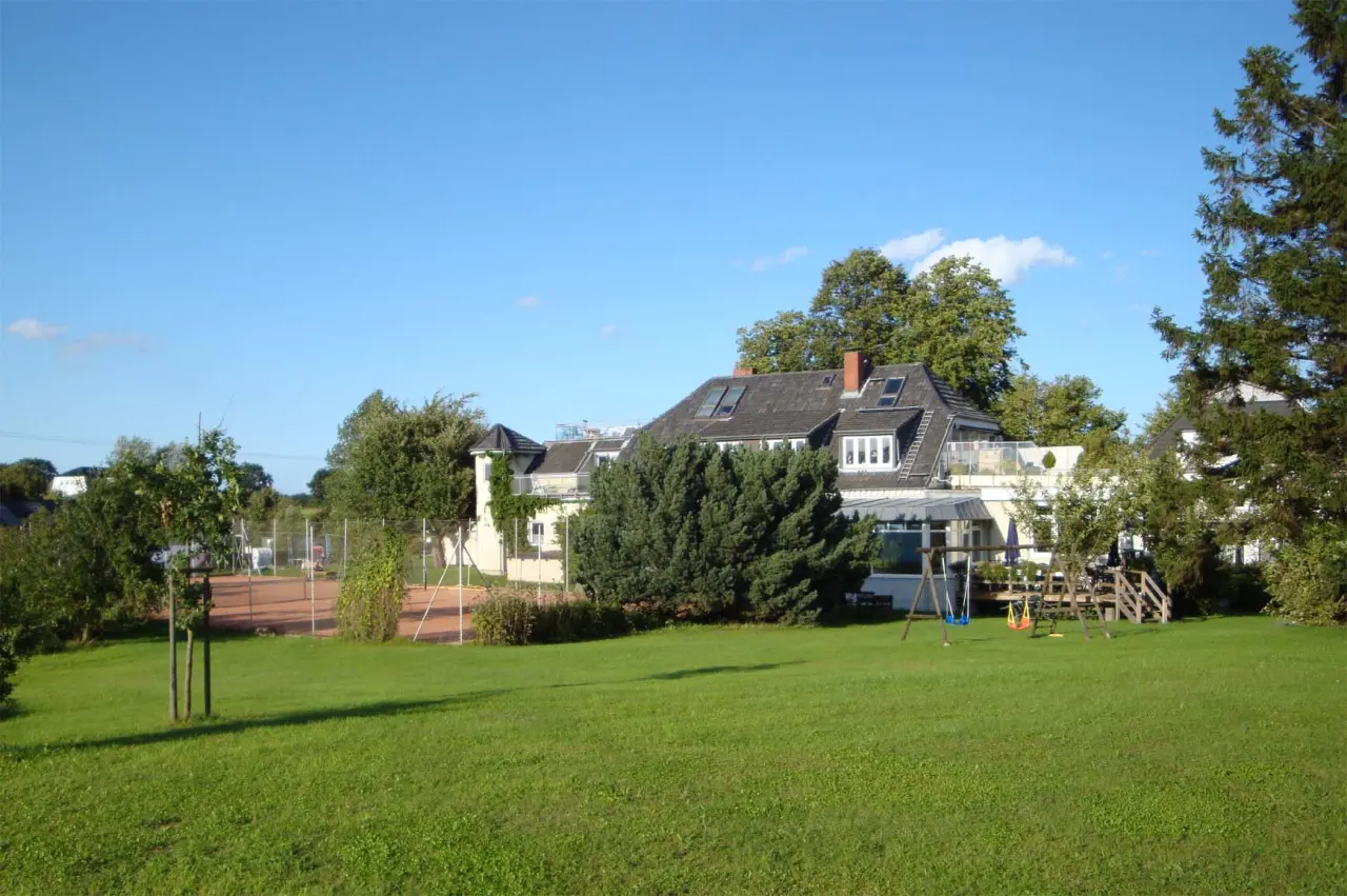 Aussenansicht des HofHotel Krähenberg mit großem Garten, Tennisplatz und Kinderspielplatz unter blauem Himmel.