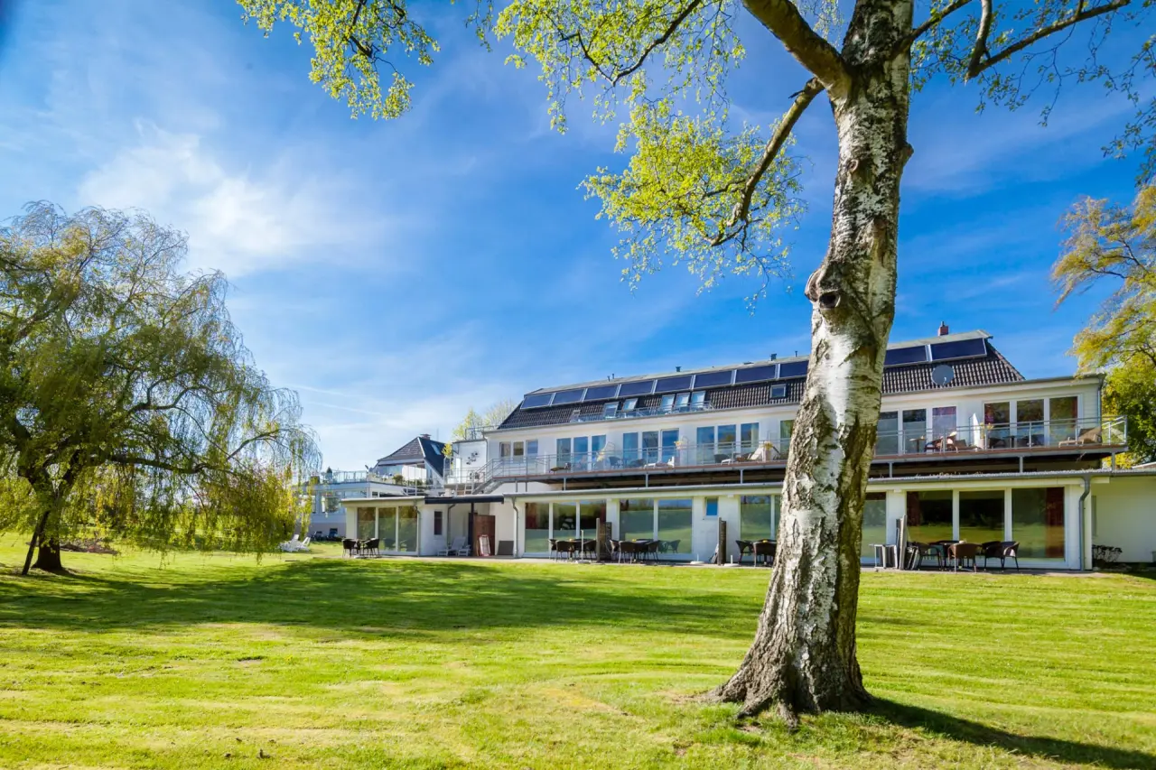 Aussenansicht des HofHotel Krähenberg mit moderner Architektur, Balkonen, grosser Rasenfläche und Bäumen unter blauem Himmel.