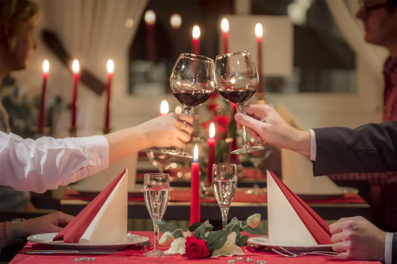 Paar stößt mit Rotwein an bei romantischem Kerzenschein-Dinner im HofHotel Krähenberg.