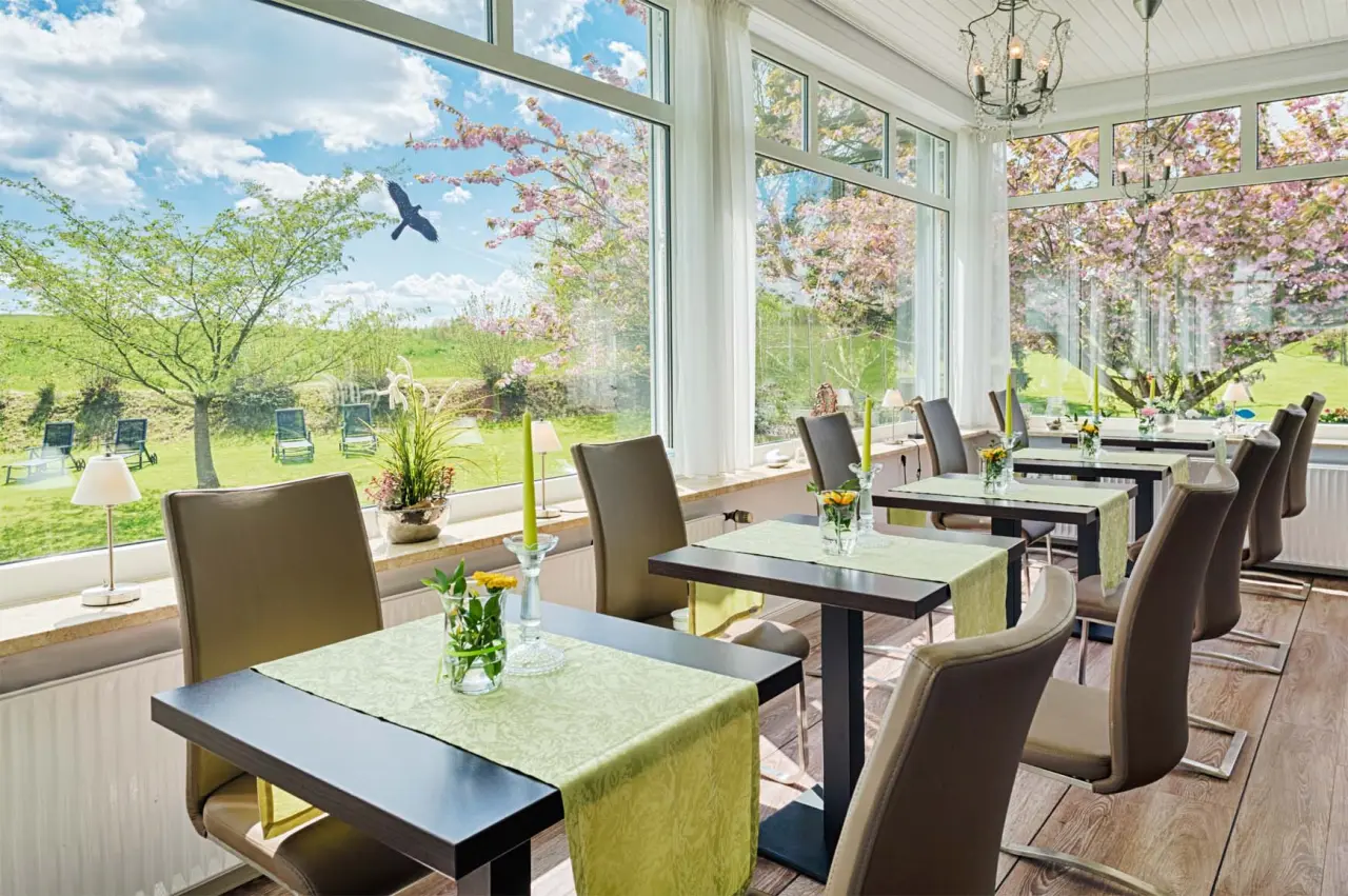 Heller Restaurantbereich im HofHotel Krähenberg mit grossen Fenstern, Blick auf blühende Bäume und grüne Landschaft.