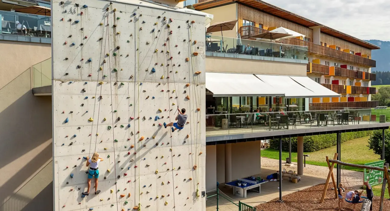 Kletterwand und Außenterrasse mit Gästen sowie Spielplatz am Aldiana Club Salzkammergut in Österreich.