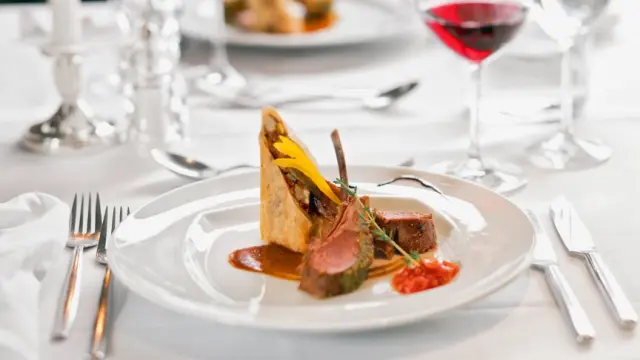 Exquisites Lammgericht mit Beilagen und Rotwein, elegant serviert im Restaurant des Aldiana Club Salzkammergut.