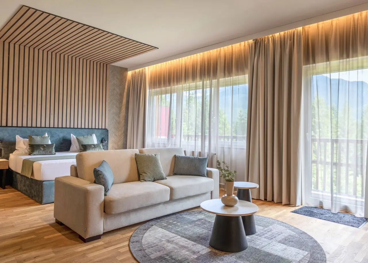Geräumige Suite im Aldiana Club Salzkammergut mit Doppelbett, Sofa und Balkonblick auf die Berge.