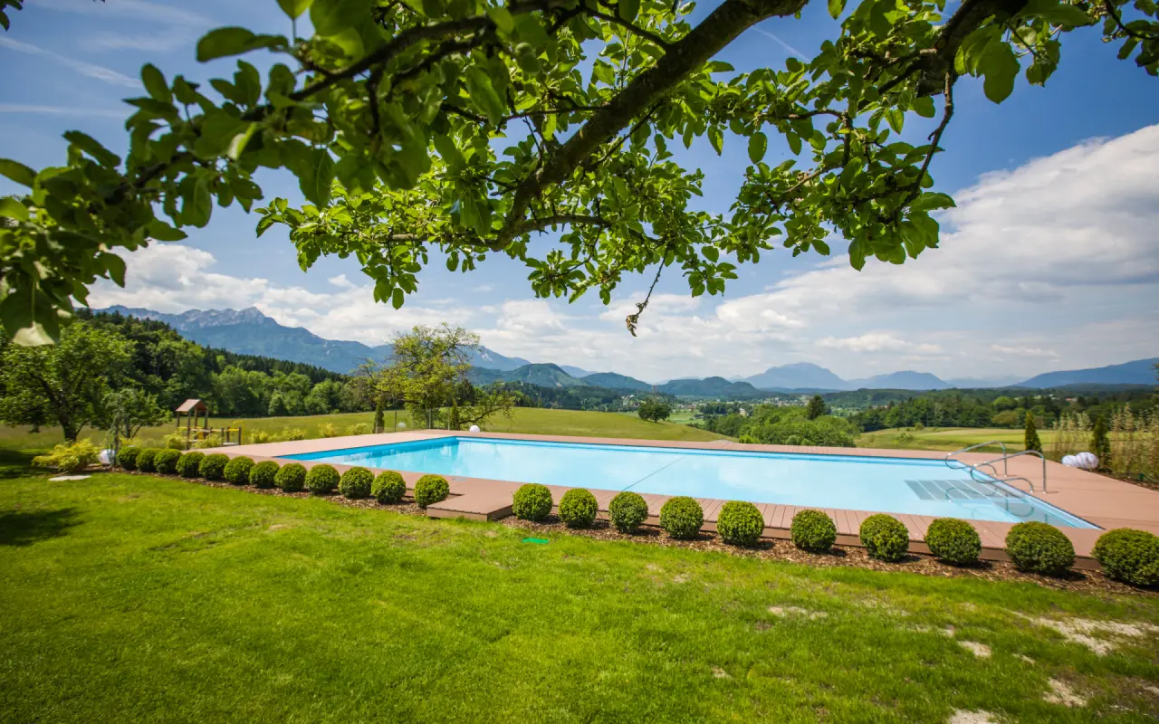 Idyllischer Aussenpool mit Holzdeck und weitem Alpenpanorama im Hotel Streklhof. Klares Wasser unter blauem Himmel.