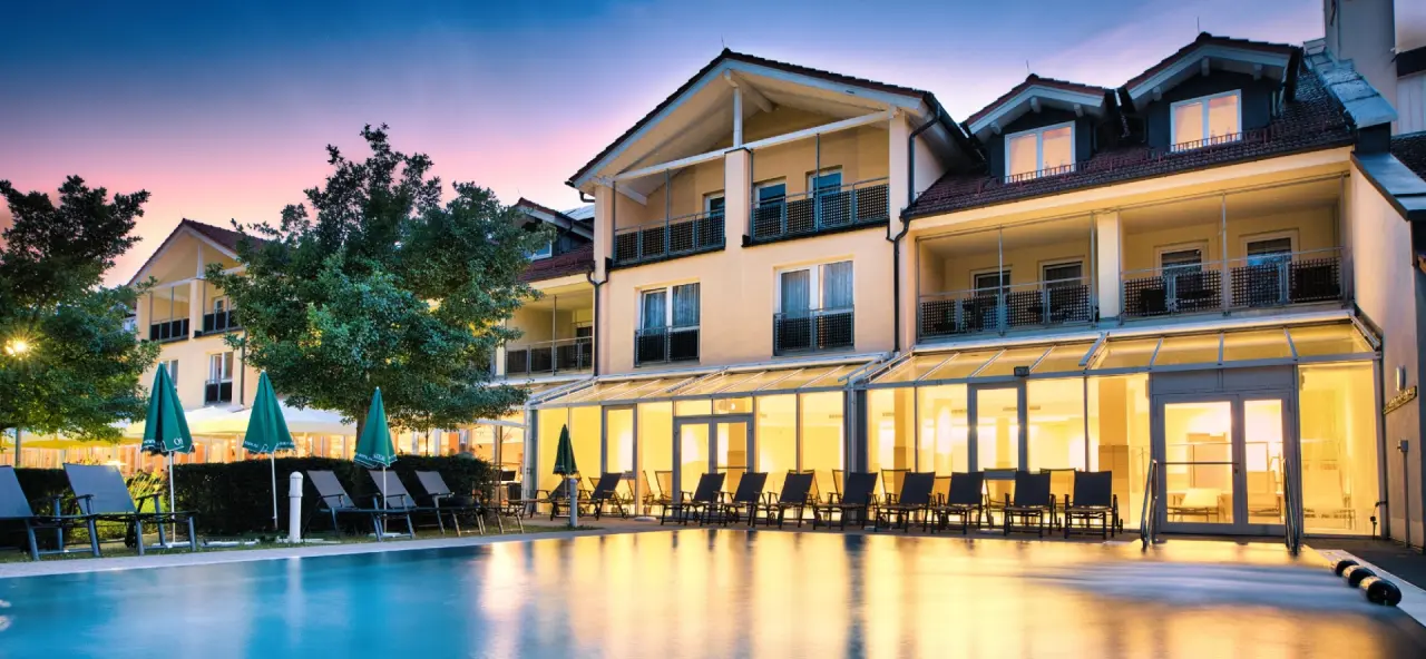 Abendliche Aussenansicht des Hotel Herzog Heinrich mit beleuchtetem Aussenpool und Liegestühlen.