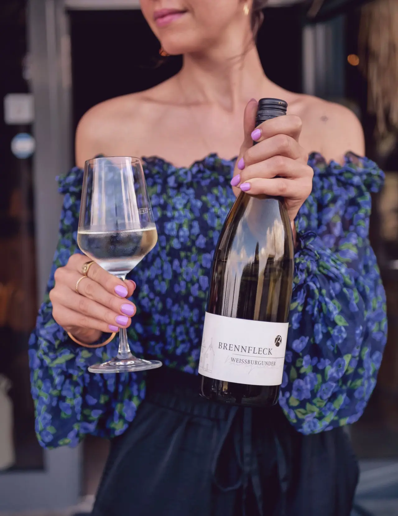 Frau hält ein Glas Weißburgunder und eine Weinflasche 'Brennfleck' im Mana Lisa Boutiquehotel.