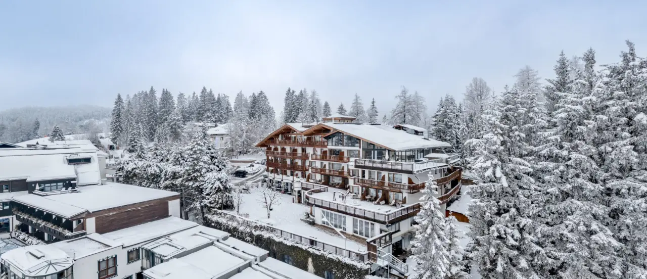 Winterliche Aussenansicht des Natur & Spa Hotel Lärchenhof, umgeben von verschneiten Tannenwäldern und Bergen.