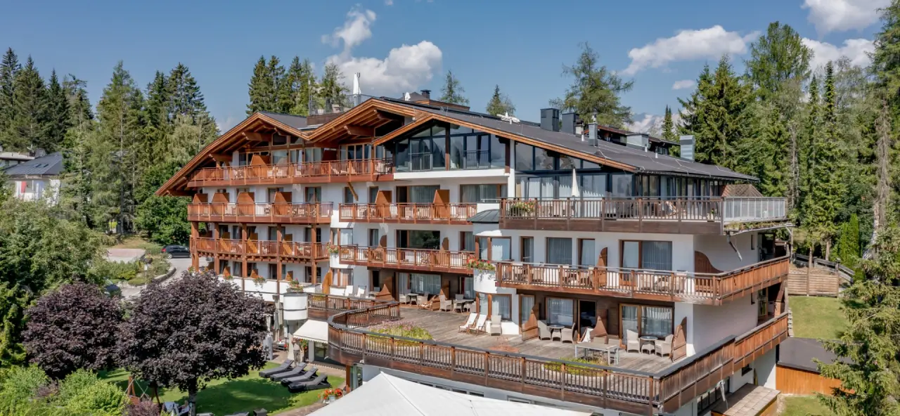 Aussenansicht des Natur & Spa Hotel Lärchenhof mit Holzfassaden und Balkonen, umgeben von grünen Bäumen unter blauem Himmel.