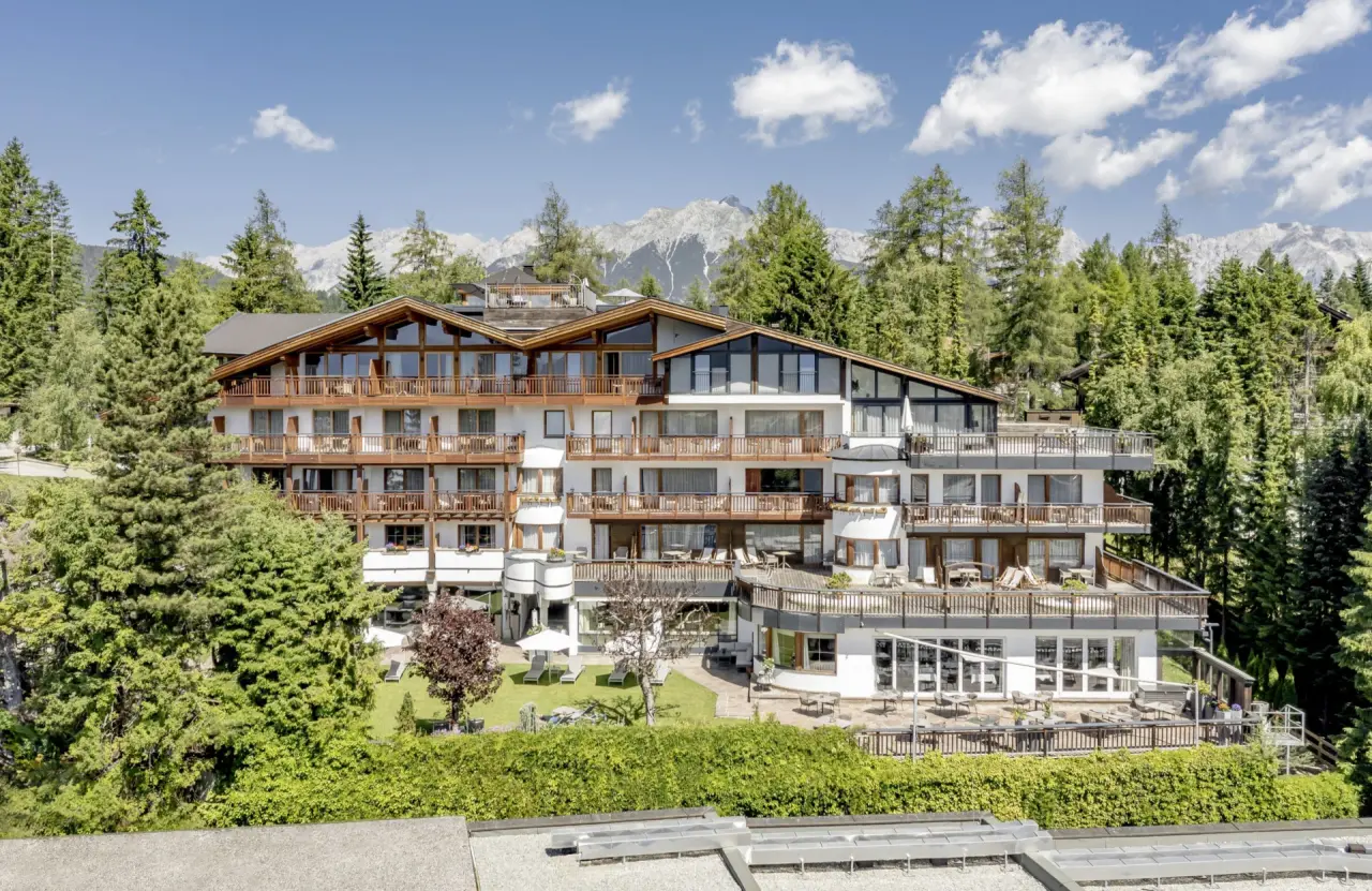 Aussenansicht des Natur & Spa Hotel Lärchenhof mit Balkonen, umgeben von Wald und Alpenpanorama unter blauem Himmel.