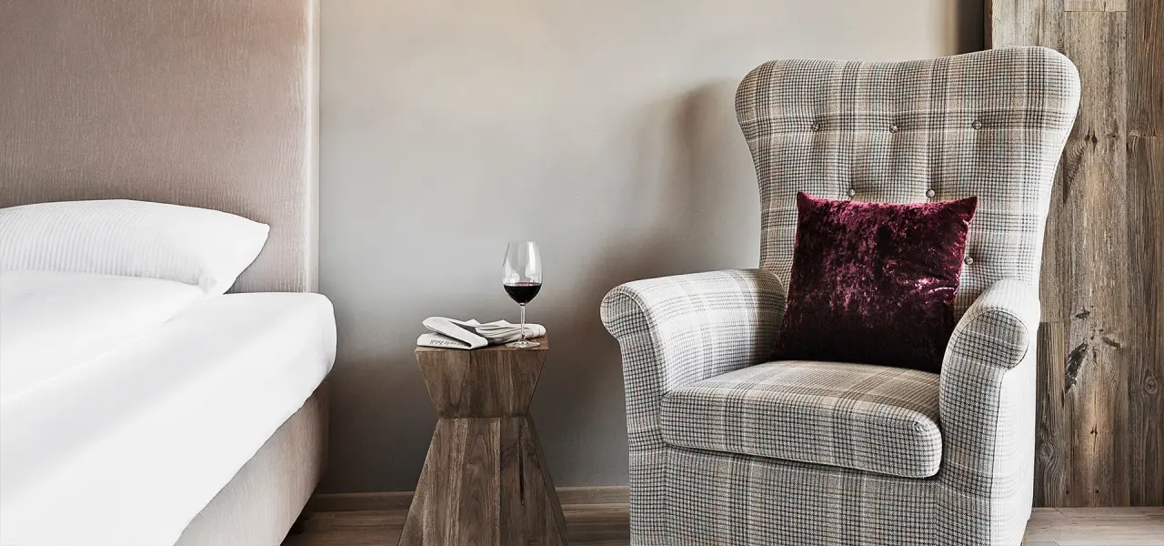 Gemütliche Sitzecke mit Sessel, Beistelltisch und Wein im Hotelzimmer des Natur & Spa Hotel Lärchenhof.