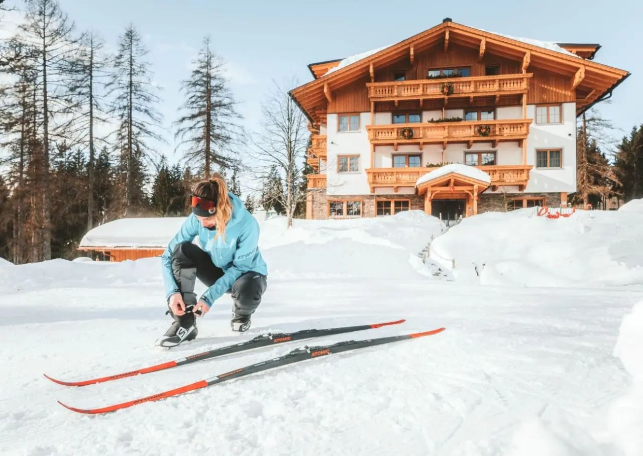 Gast beim Langlauf vor dem Hotel Lindenhof in verschneiter Alpenlandschaft. Winterurlaub mit traditioneller Architektur.